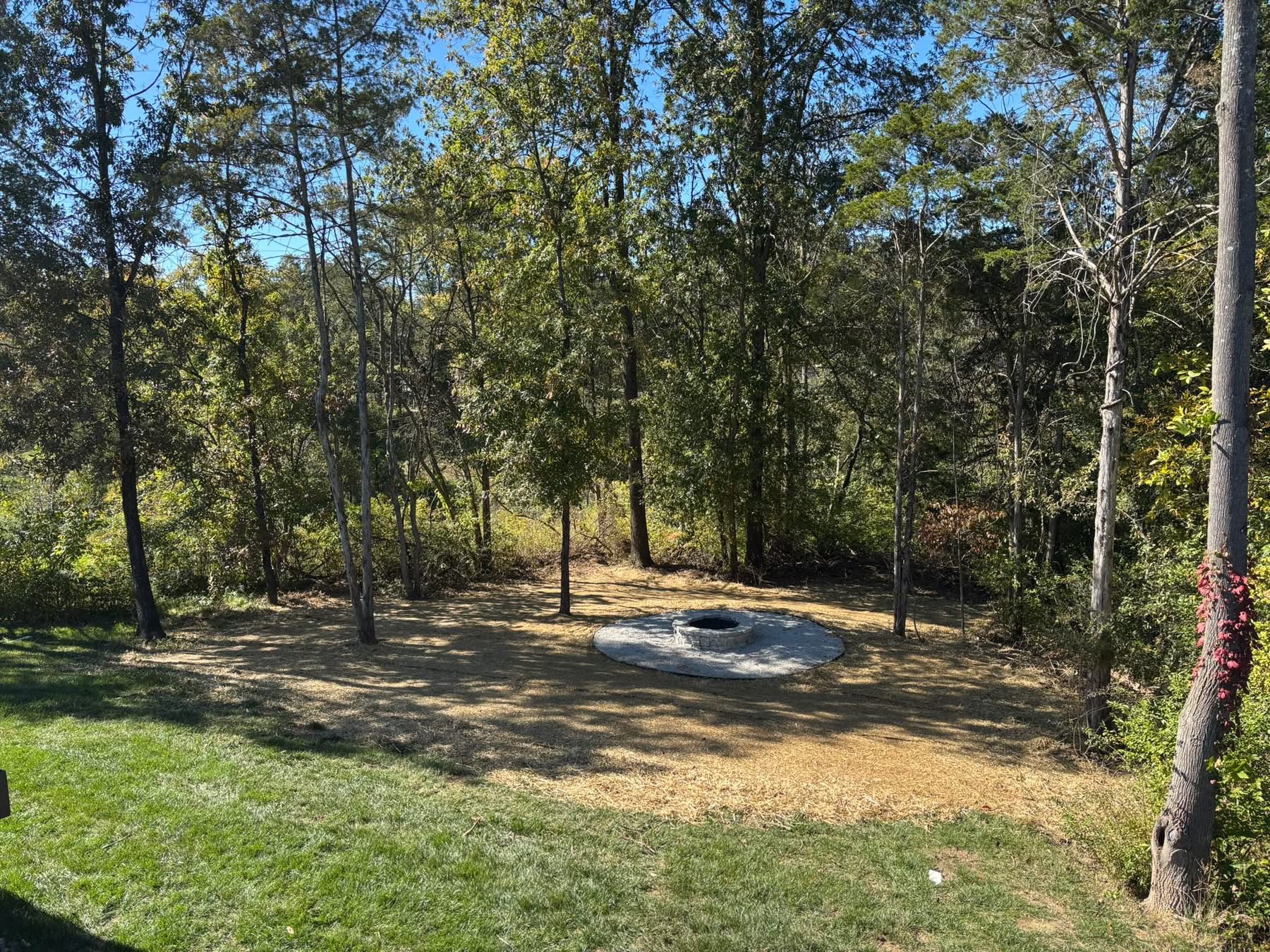 Custom backyard fire pit patio with decorative gravel and natural wooded backdrop