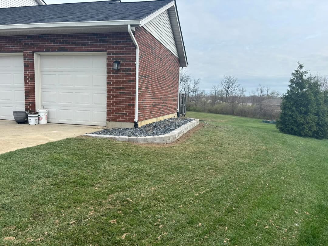 Decorative rock bed with stone retaining border installed along garage foundation