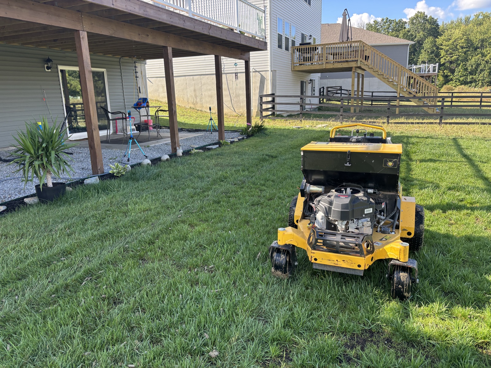 Yellow zero-turn stand-on mower cutting residential backyard lawn