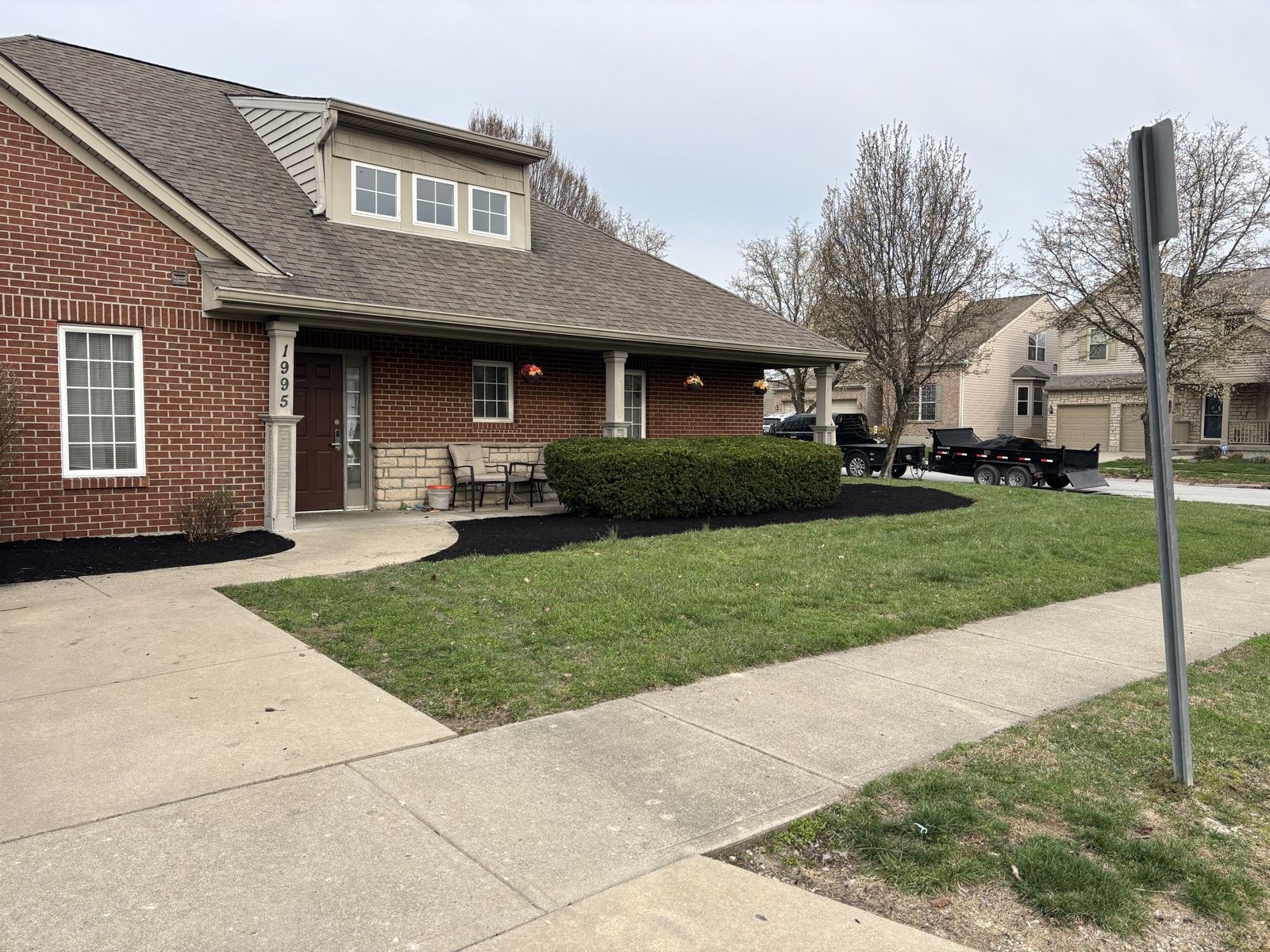 Brick home with freshly installed dark mulch beds — Hunley dump trailer on site